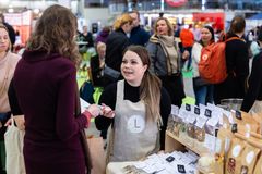 Nainen keskustelee myyntipöydän takana asiakkaan kanssa ruokamessuilla täynnä kävijöitä.