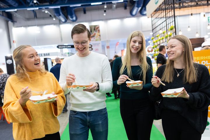 Neljä ihmistä nauttimassa ruokaa messuilla yhdessä.