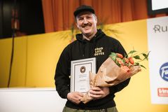 Kuvassa henkilö hymyilee pitäen käsissään kukkakimppua ja palkintoa. Taustalla on keltainen seinä ja oranssi verho.