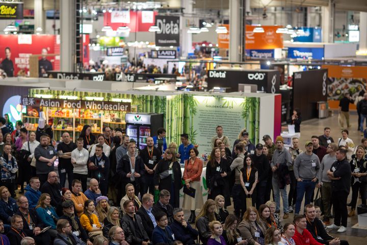 Ihmisiä seisoo ja istuu messukeskuksessa Gastro Helsinki -messujen näyttelyosastojen edessä. Taustalla näkyy kylttejä.