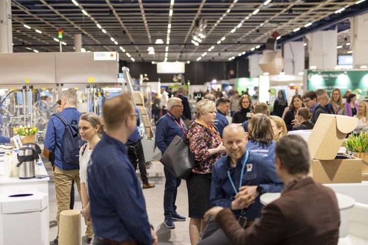 Messuhallissa on paljon ihmisiä keskustelemassa ja tutustumassa erilaisiin esittelypisteisiin.