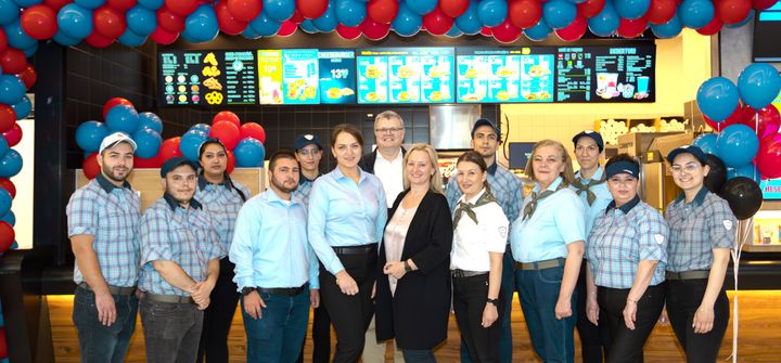 Kuvassa Hesburger Râmnicu Vâlcean avaustiimi sekä Hesburgerin toimitusjohtaja Kari Salmela (keskellä takana) ja Hesburgerin kansainvälisten asioiden kehitys- ja markkinointijohtaja Ieva Salmela (keskellä edessä).