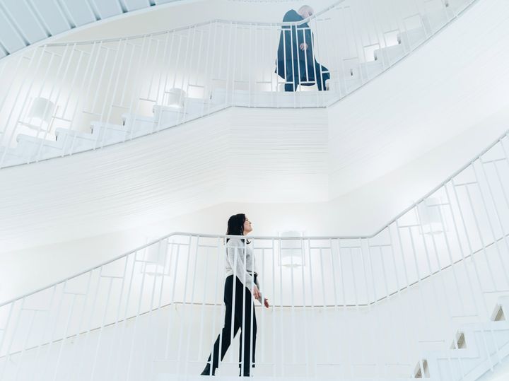Nainen ja mies kävelevät eri kerroksissa valkoisessa modernissa portaikossa.