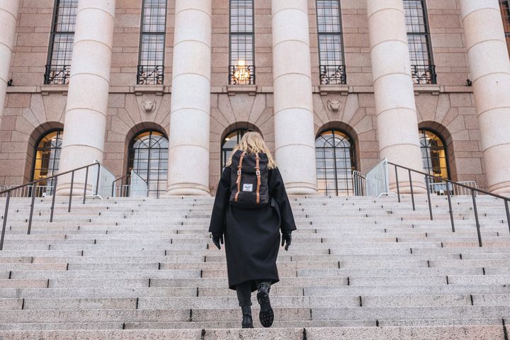 Henkilö kävelee ylös suuria portaita kohti suurta rakennusta pylväineen.