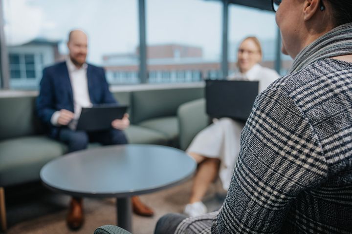 Kolme henkilöä istuu toimistoympäristössä keskustelemassa.