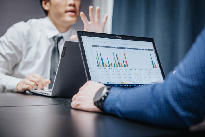 Kaksi henkilöä kokouksessa, kannettavilla tietokoneilla näkyy värikkäitä graafeja.