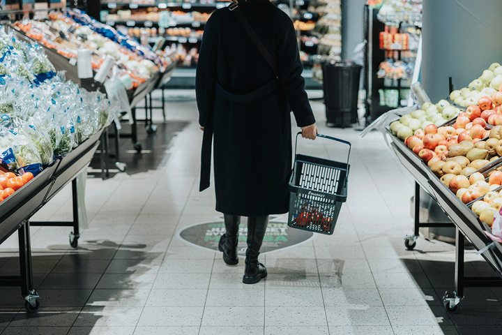 Henkilö kävelee ostoskorin kanssa kaupan vihannesosastolla.