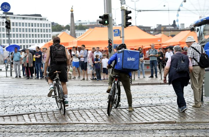 Kaksi pyöräilijää ajaa kiveyksellä Helsingin torilla, taustalla oransseja telttoja ja ihmisjoukko.
