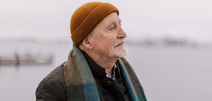 An old man dressed in winter clothes looks into the distance.