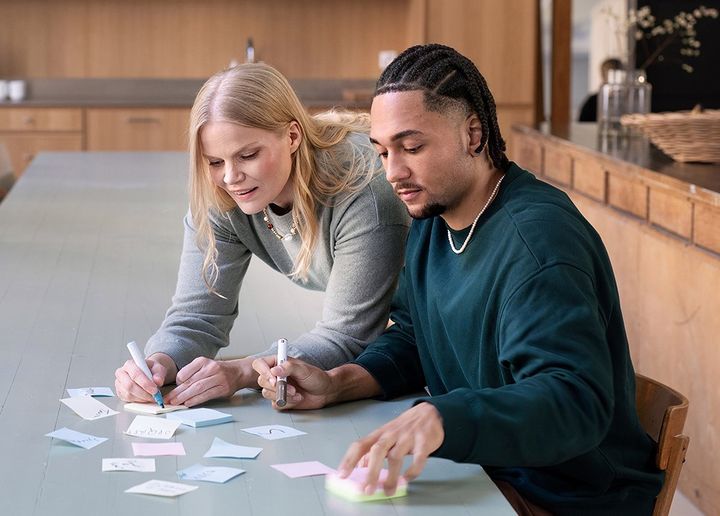 Kaksi ihmistä täyttää muistilappuja pöydän ääressä.