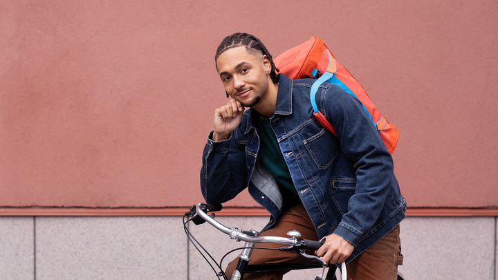 Nuori aikuinen nojaa reppu selässä polkupyörän ohjaustankoon.