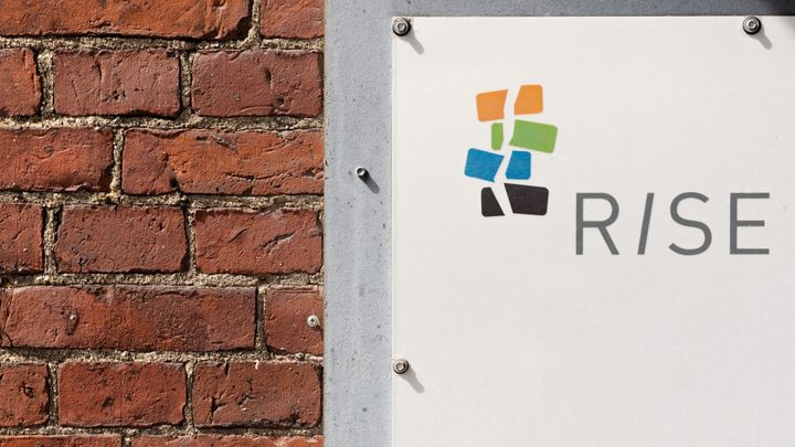 Tiiliseinä, johon on kiinnitetty Rikosseuraamuslaitoksen logo. Logossa on neljä tiilenkaltaista muotoa pinossa ja sana RISE.