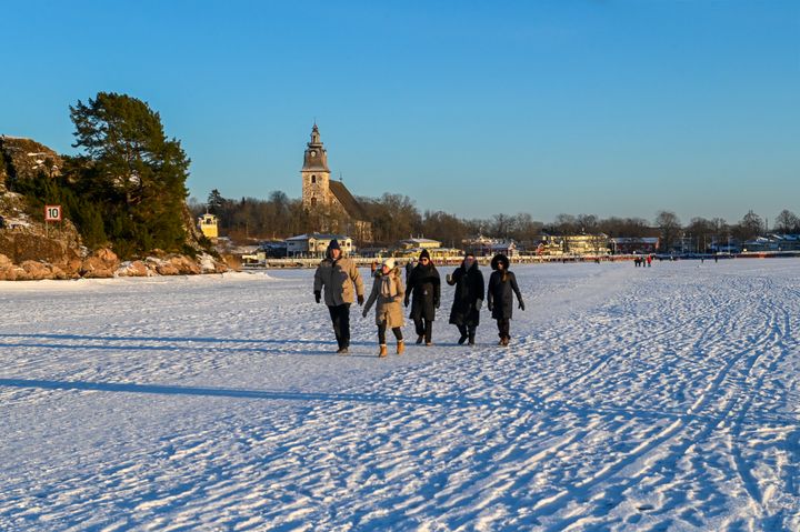 Ihmisiä kävelemässä meren jäällä aurinkoisena päivänä. Taustalla Naantalin kirkko ja vierasvenesatama.