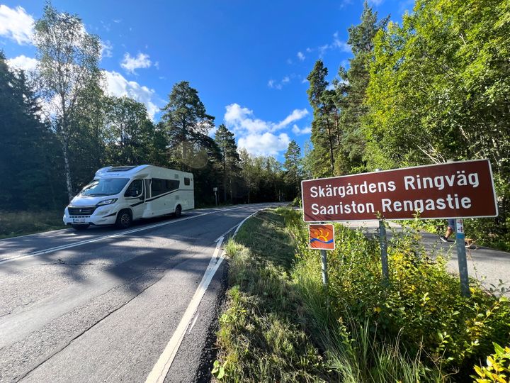 Saariston rengastie -kyltti maantien varressa ja vastaan tuleva matkailuauto.