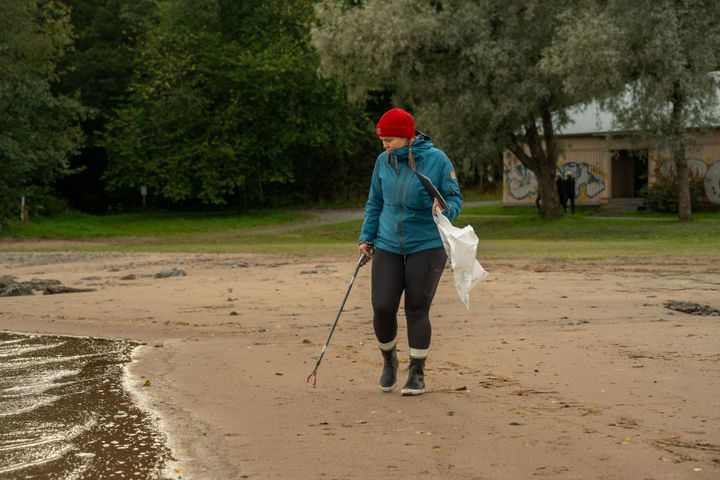 Henkilö siivoaa ranta-aluetta roskapihdeillä.