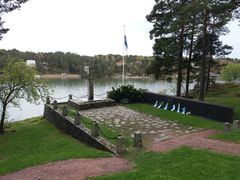 Kivinen muistomerkki, lipputanko ja muistoseinä meren rannalla.