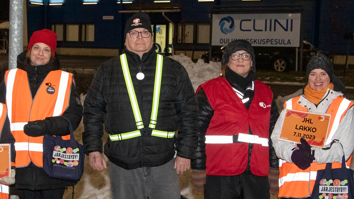 Members of Trade Union JHL wearing colourful strike vests outside Oulun keskuspesula, dark morning.