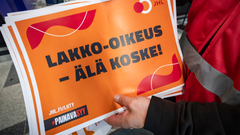 Oranssi JHL:n lakkokyltti työntekijän kädessä.