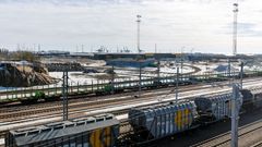 Train cars in a sunny rail yard, port cranes in the background.