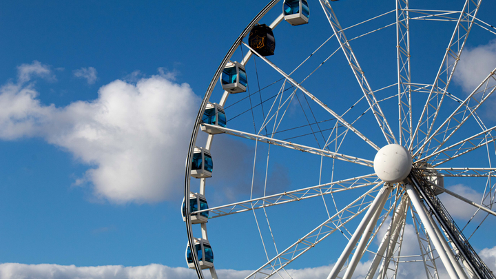 Kuvassa maailmanpyörä Sky Wheel Helsingissä Katajanokalla, taustalla sininen taivas ja muutamia poutapilviä