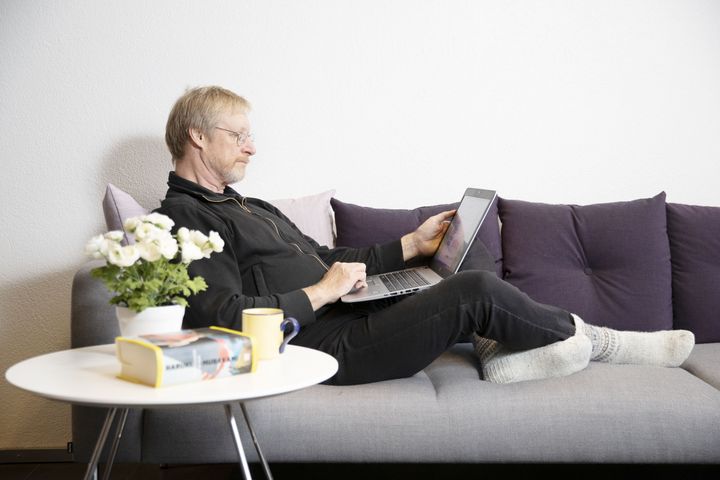 Mies istuu sohvalla kannettava tietokone sylissään.