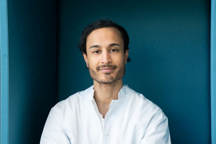 Rahul Raj in a white shirt looking at the camera against a blue background.