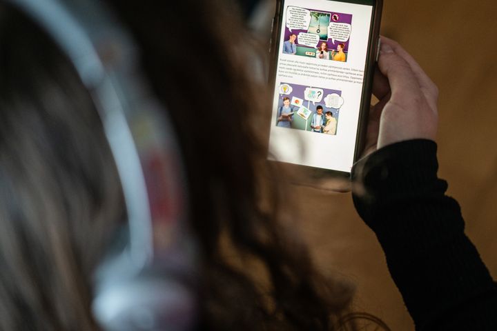 Nuori katsoo puhelimellaan sarjakuvaa, jossa on puhekuplia.