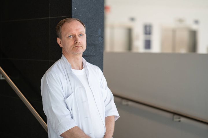 En man i vit skjorta står vid en vägg i en modern byggnadsinteriör.