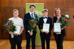 Neljä henkilöä seisoo rivissä ja pitävät palkintodiplomeja ja kukkakimppuja. Taustalla on vihreä juliste.