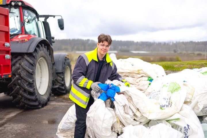Nuori työskentelee maatalousmuovien keräyspisteellä ison traktorin edessä.
