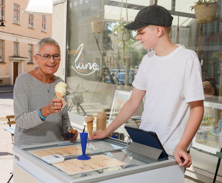 Nuori yrittäjä myy jäätelöä vanhemmalle naiselle kioskin edessä.