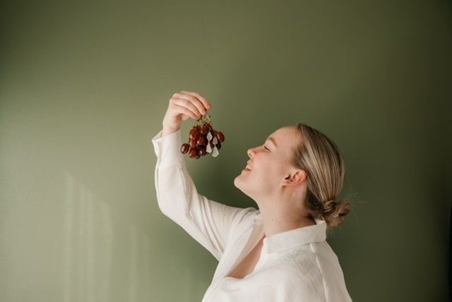 Nainen nostaa rypäletertun huulilleen vihreän seinän edessä.