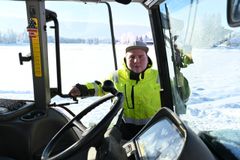 Henkilö seisoo traktorin oven vieressä lumisessa maisemassa.