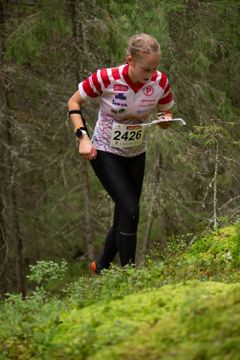 Nuori nainen suunnistusvaatteissa juoksee metsässä kartta kädessään.
