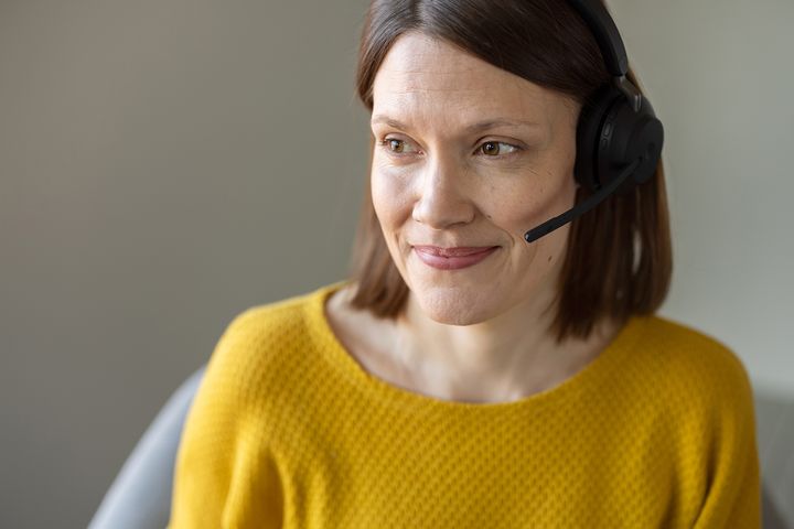 Nainen keltaisessa paidassa ja hands-free-kuuloke päässään.