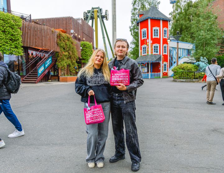 Kaksi henkilöä seisoo yhdessä iloisesti Linnanmäen huvipuistossa.