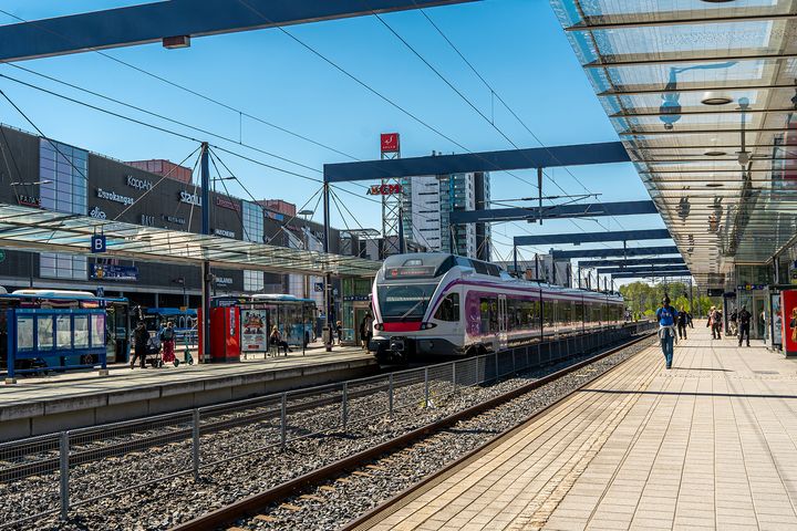 A train is arriving at the Leppävaara railway station on a sunny summer day. The Sello shopping centre is in the background.