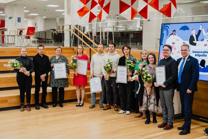 A group of 11 people pose with certificates of honour and flowers in their hands.