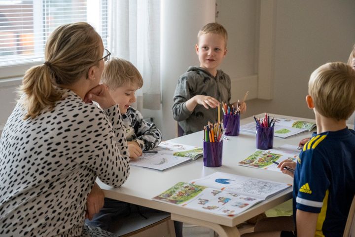Lapset tekevät tehtäväkirjan tehtäviä pöydän ääressä opettajan johdolla.