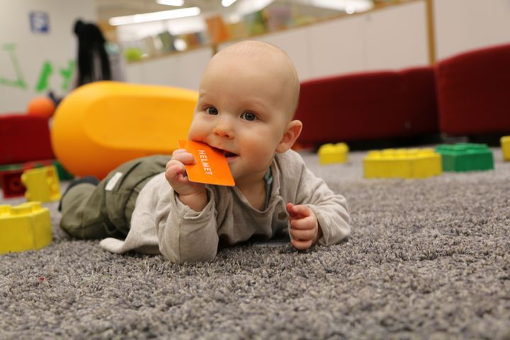 Iloinen vauva kirjastossa Helmet-kirjastokortti suussa.