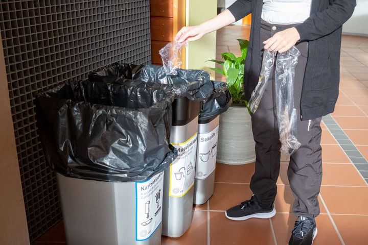 Lajitteluastioita ja henkilö laittamassa muovijätettä omaan lajitteluastiaan.
