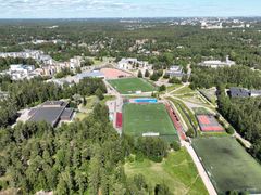 Ilmakuva, jossa näkyy rakennuksia, jalkapallokenttiä ja metsikköä.