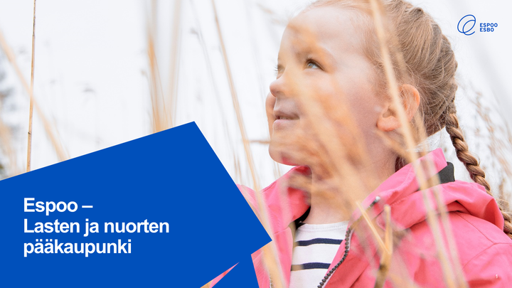 Lettipäinen tyttö hymyilee heinikossa. Kuvassa tekstikenttä, jossa lukee: Espoo - Lasten ja nuorten pääkaupunki,