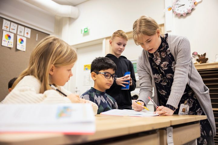 Espoolaisia koululaisia ja opettaja katsovat luokassa sivua oppilaan koulukirjasta.