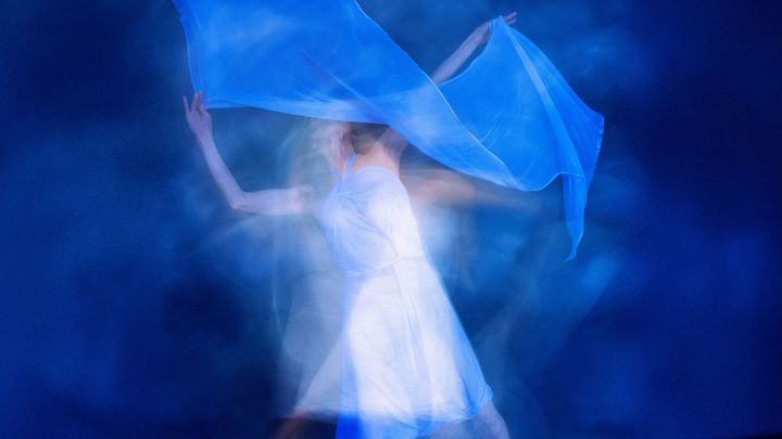 Valkoiseen asuun pukeutunut henkilö tanssii ja heiluttelee käsissään valkoisia huiveja.