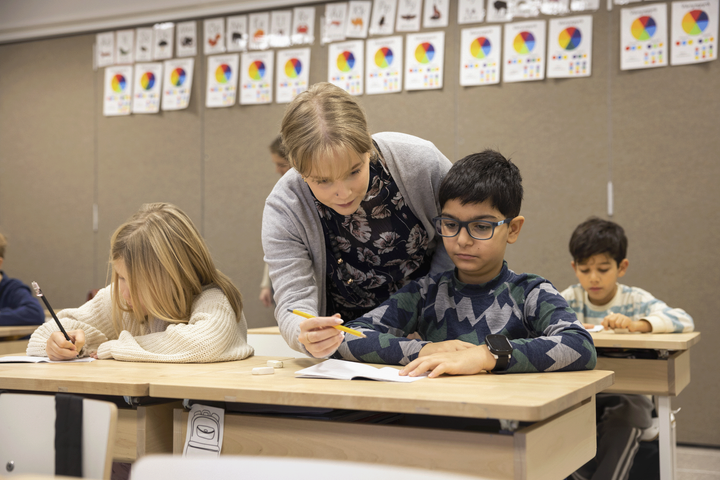 Opettaja neuvoo pulpetin ääressä opiskelevaa oppilasta.