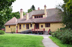 Keltainen jugendrakennus puutarhan ympäröimänä kesällä.