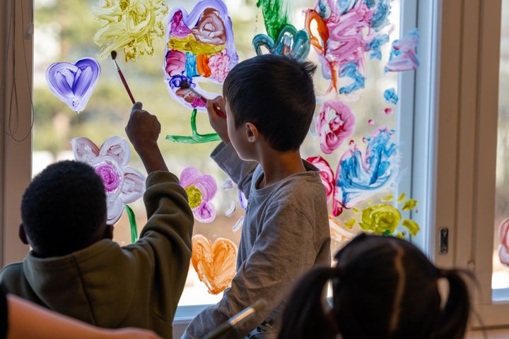 Päiväkodissa lapsia maalaamassa sormiväreillä taidetta ikkunaan.