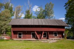 Punainen aittarakennus aurinkoisella ilmalla nurmikkoalueen reunassa.