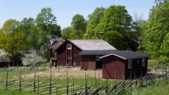 Kolme punaista puutaloa niityn takaa kuvattuna aurinkoisena kesäpäivänä.